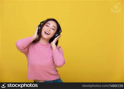 Happy cheerful Beautiful Asian woman wearing wireless headphones enjoying listening to music on yellow background.People lifestyle concept