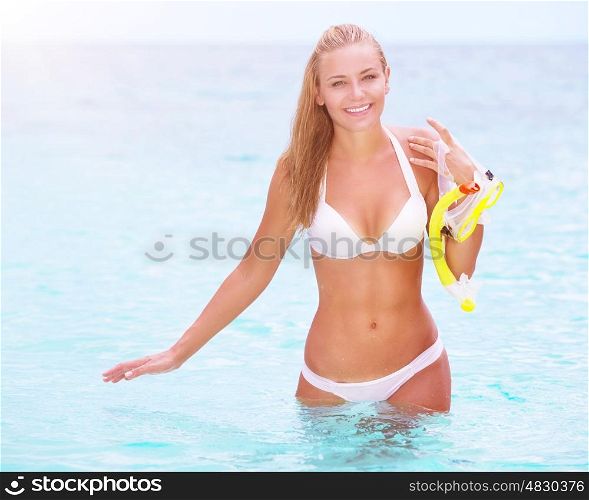 Happy cheerful beautiful girl walking out of the water with snorkeling mask in hands, having fun on the beach, enjoying summer watersport