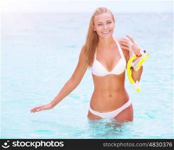 Happy cheerful beautiful girl walking out of the water with snorkeling mask in hands, having fun on the beach, enjoying summer watersport