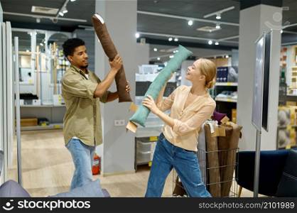 Happy cheerful couple fighting with cushion in store. Overjoyed man and woman having fun on shopping. Cheerful couple fighting with cushion in store