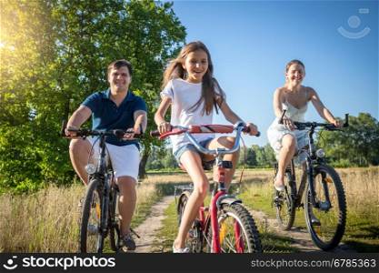 Happy cheerful family with daughter riding bicycles in meadow at sunny day