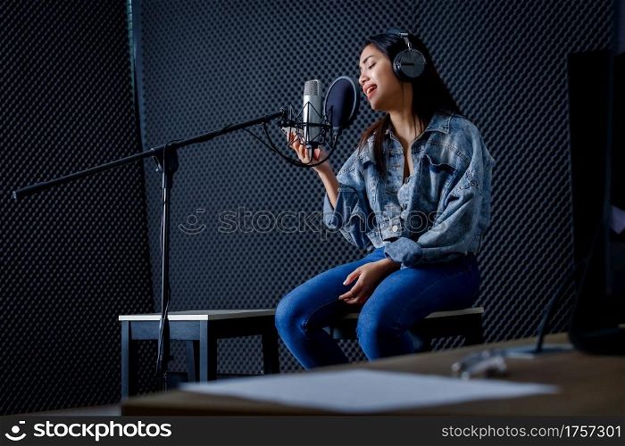 Happy cheerful pretty smiling of portrait of young Asian woman look at the smartphone vocalist Wearing Headphones recording a song front of microphone in a professional studio