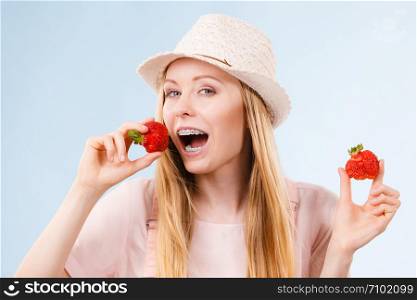 Happy cheerful teenage young woman ready for summer wearing pink outfit and sun hat holding sweet fruit red strawberries. Happy woman holding strawberries