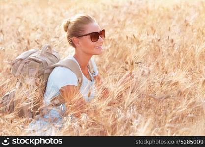 Happy cheerful woman sitting in beautiful golden wheat field, travel with backpack along Europe, active lifestyle concept