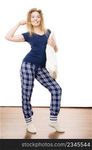 Happy cheerful woman wearing blue pajamas holding pillow and toothbrush, sleep outfit blue tshirt and checked trousers. Happy cheerful woman wearing pajamas
