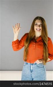 Happy cheerful woman with long brown hair gesturing waving hand, welcoming somebody.. Happy woman gesturing with hand