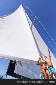 Happy cheerful young couple standing on the deck of sailboat and dreamy looking up in the sky, enjoying honeymoon vacation, romantic summer holidays