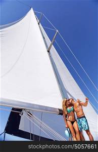 Happy cheerful young couple standing on the deck of sailboat and kissing, enjoying honeymoon vacation, romantic summer holidays