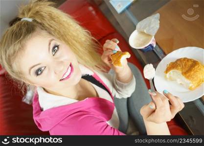 Happy cheerful young teenage woman eating croissant bun and cottage cheese yoghurt. Woman eating croissant and yoghurt
