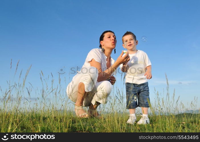 happy child and woman outdoor playing with soap bubble on meadow