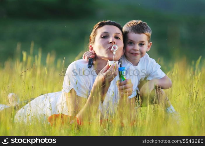 happy child and woman outdoor playing with soap bubble on meadow