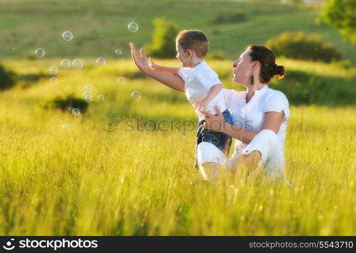 happy child and woman outdoor playing with soap bubble on meadow