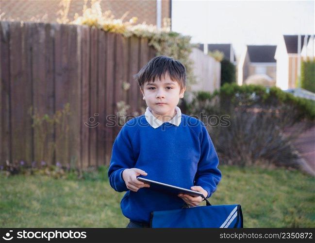 Happy Child boy holding tablet pc standing outside waiting for School bus, Portrait Kid playing game online or reading strory on internet, Preschool boy learning with modern technology
