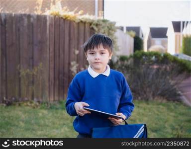 Happy Child boy holding tablet pc standing outside waiting for School bus, Portrait Kid playing game online or reading strory on internet, Preschool boy learning with modern technology