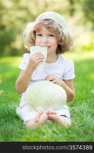 Happy child eating cabbage against green spring background