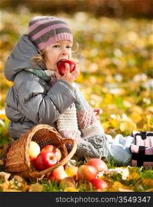 Happy child eating red apple in autumn park. Healthy lifestyles concept