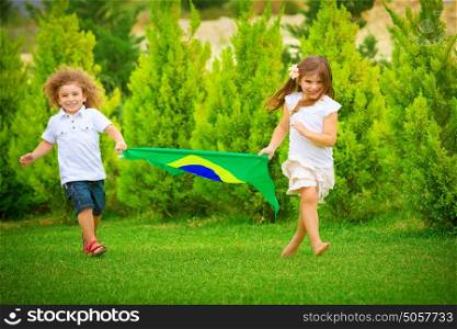 Happy child enjoying football championship, brother and sister running with big Brazil flag, active and sportive childhood concept