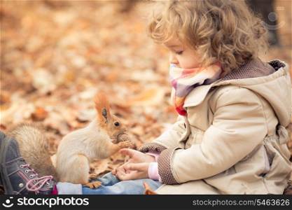 Happy child feeds a little squirrel in autumn park