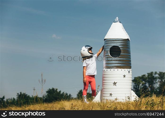 Happy child girl dressed in an astronaut costume playing with hand made rocket. Summer outdoor. Happy child girl dressed in an astronaut costume playing with hand made rocket. Summer outdoor.