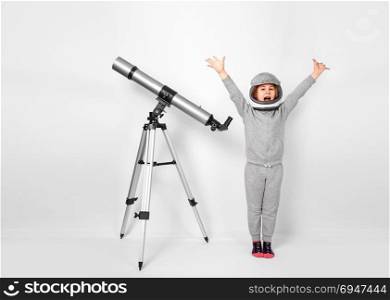 Happy child girl dressed in an astronaut costume standing beside the telescope. Happy child girl dressed in an astronaut costume standing beside the telescope.