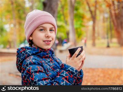 Happy child girl in the park resting with hot tea on a walk, autumn cozy mood. Portrait of a child with a cute smile and braces.. Happy child girl in the park resting with hot tea on a walk, autumn cozy mood.