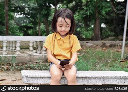 Happy child girl using mobile smartphone in the park. Kid is looking at screen of devices. Concept of communication, technology.