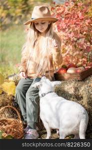 Happy child girl with white dog playing little farmer in autumn garden