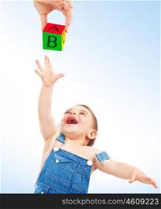 Happy child having fun, cute cheerful little boy stretches to take cube with the letters from mother's hand over clean blue-white background, enjoying education&#xA;