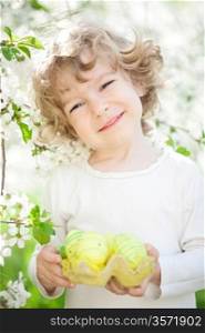 Happy child holding Easter eggs against spring flower background