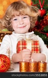 Happy child holding gift box against Christmas tree with decorations