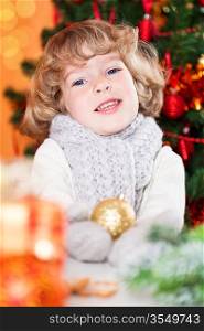 Happy child holding gold ball against Christmas tree with decorations