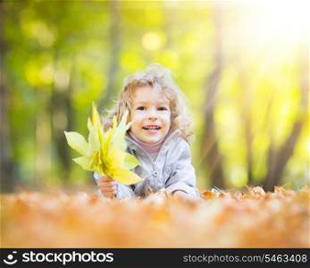 Happy child holding yellow leaves in autumn park