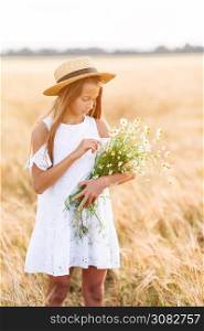 Happy child in wheat field. Beautiful girl in white dress in a straw hat with a bouquet of chamomile in hands. Happy child in wheat field. Beautiful girl in white dress in a straw hat with ripe wheat in hands