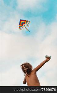 Happy child launches a kite, baby looking up at a multi-colored kite soaring in the sky, happy childhood, kid enjoying summer holidays, photo with copy space, freedom concept