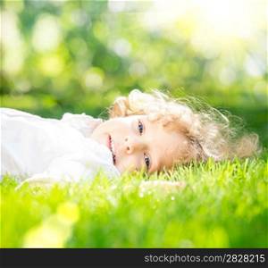 Happy child lying on green grass against spring sunny background