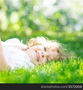 Happy child lying on green grass outdoors in spring park