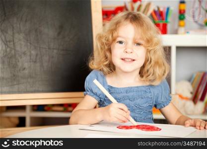 Happy child painting heart on a paper in class. School concept