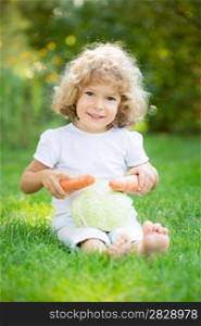 Happy child playing with vegetables on green grass outdoors in spring park