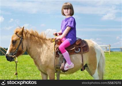 happy child ride farm animal brown pony with blue sky in background and beautiful nature