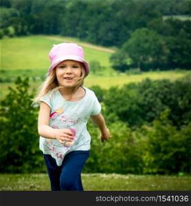 Happy child running in summertime. Adorable kid jogging and smiling. pretty Toddler in sports action. front of lovely little girl expressing energy in meadow. Active carefree caucasian child portrait.