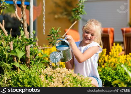 Happy child watering flowers in the garden in front of her home