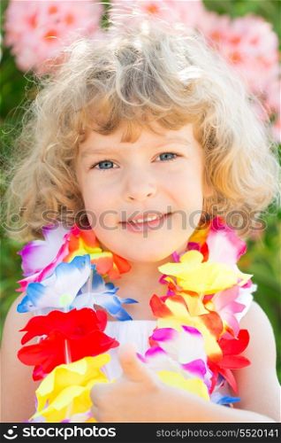 Happy child wearing hawaiian flowers garland showing thumb up sign on the beach. Summer vacations concept