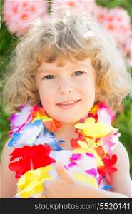 Happy child wearing hawaiian flowers garland showing thumb up sign on the beach. Summer vacations concept