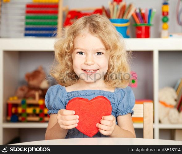 Happy child with handmade paper red heart in class. School concept