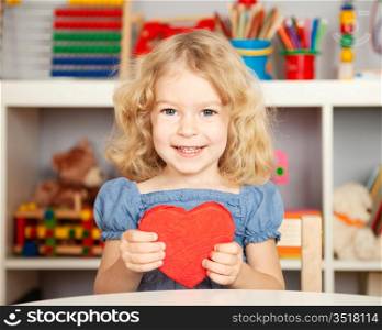 Happy child with handmade paper red heart in class. School concept