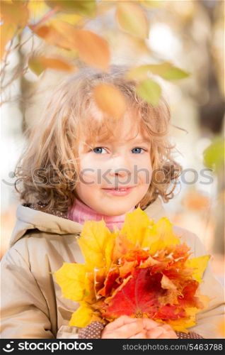 Happy child with maple leaf in autumn park against yellow blurred leaves background