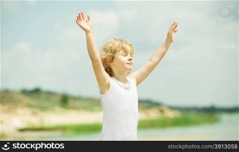 Happy child with raised arms standing near the sea. Vacation concept