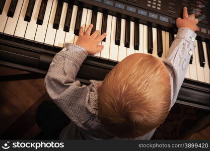 Happy childhood and music. Little boy child kid playing on the black digital midi keyboard piano synthesizer musical instrument indoor.