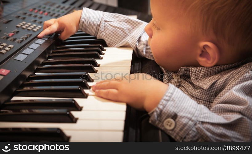 Happy childhood and music. Little boy child kid playing on the black digital midi keyboard piano synthesizer musical instrument indoor.