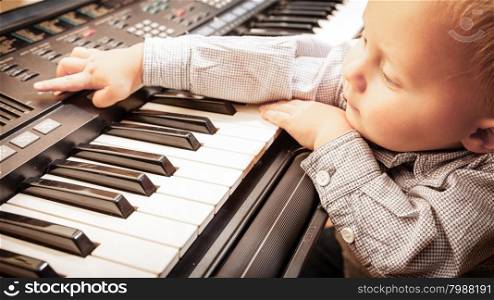 Happy childhood and music. Little boy child kid playing on the black digital midi keyboard piano synthesizer musical instrument indoor.